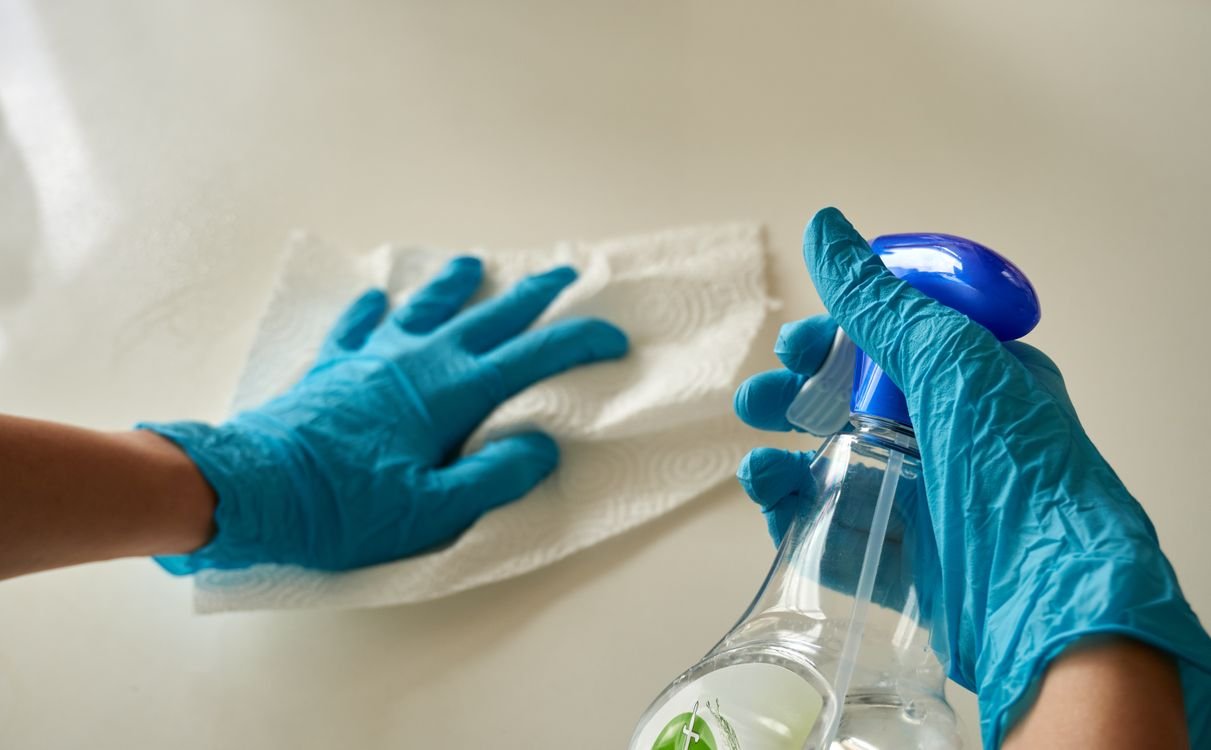 Gloved hands cleaning a surface with a spray bottle and cloth